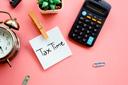 a desk with a laptop and financial documents, holding a pen and reviewing paperwork, representing a stress-free approach to a stress free tax season.
